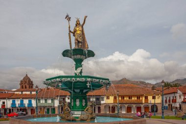CUSCO, PERU - 30 Nisan 2022: Peru 'daki Cusco Plaza de Armas' daki su çeşmesinin üzerinde duran İnka İmparatoru Manco Capac 'a adanmış heykel. Sol tarafta İsa Cemiyeti Kilisesi duruyor..