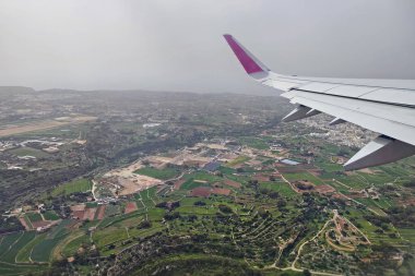 Malta - February 28, 2024: Clouds and a wing of Wizzair airbus from the airplane window. over  Malta towns  clipart