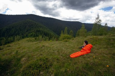 Turuncu uyku tulumundaki kadın Karpat dağlarında yeşil çimlerin üzerinde