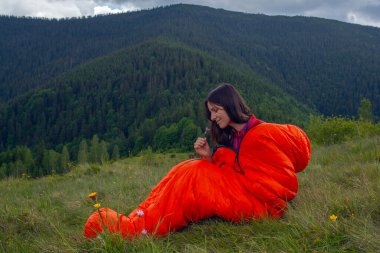 Turuncu uyku tulumundaki kadın Karpat dağlarında yeşil çimlerin üzerinde