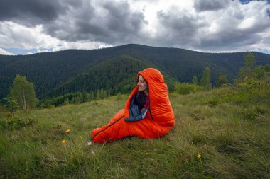Turuncu uyku tulumundaki kadın Karpat dağlarında yeşil çimlerin üzerinde