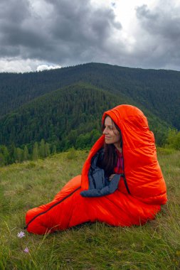 Turuncu uyku tulumundaki kadın Karpat dağlarında yeşil çimlerin üzerinde