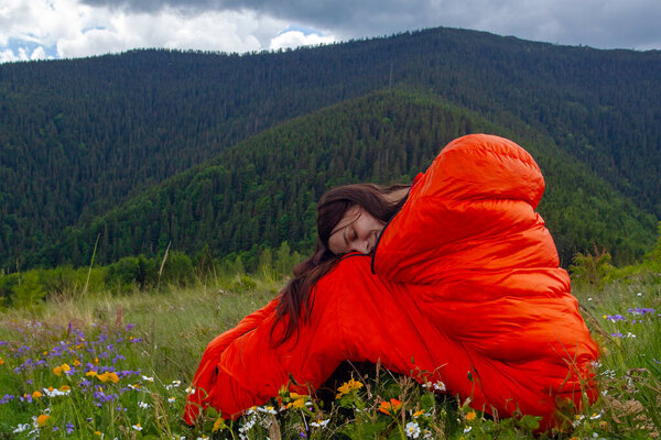 Woman tourist in orange sleeping bag  on green grass in Carpathian mountains