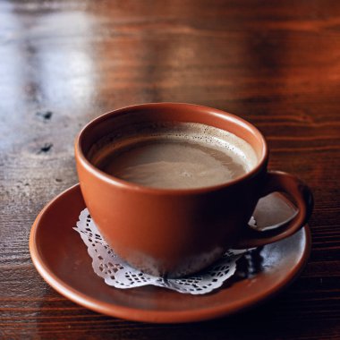 Taze Americano kahvesi. Sütlü, geleneksel kahverengi kilden bardakta, ahşap masada.