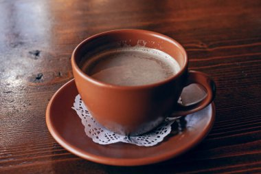 Taze Americano kahvesi. Sütlü, geleneksel kahverengi kilden bardakta, ahşap masada.