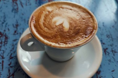 Taze aro, mavi ahşap masasında kalp köpüğü olan kapuçino.