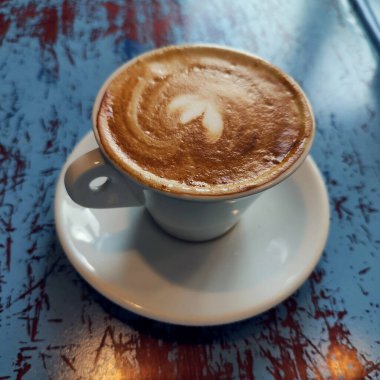 Taze aro, mavi ahşap masasında kalp köpüğü olan kapuçino.