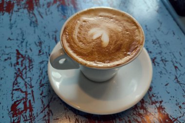 Taze aro, mavi ahşap masasında kalp köpüğü olan kapuçino.