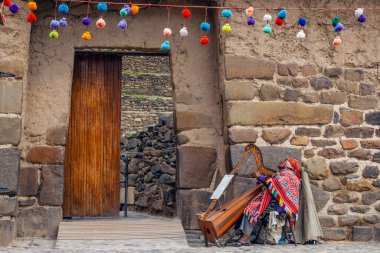 Ollantaytambo, Peru - 5 Mayıs 2022: Geleneksel elbiseli Inka adam, Ollantaytambo antik şehir kalesinin girişinde arpta müzik çalıyor