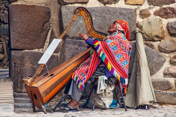 Ollantaytambo, Peru - 5 Mayıs 2022: Geleneksel elbiseli Inka adam, Ollantaytambo antik şehir kalesinin girişinde arpta müzik çalıyor