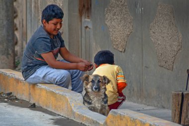 Ollantaytambo Peru - May 5, 2022:  Local Peruvian Children playing with dog  on the street in Ollantaytambo , ancient town with traditional architecture clipart