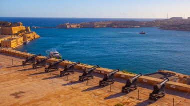 Valletta, Malta - February 13, 2024:  Cannons of the Saluting Battery point out over the Grand Harbour and Fort St Angelo, on a clear morning, Upper Barrakka Gardens, Capital city of Malta, clipart