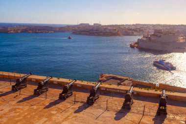 Valletta, Malta - February 13, 2024:  Cannons of the Saluting Battery point out over the Grand Harbour and Fort St Angelo, on a clear morning, Upper Barrakka Gardens, Capital city of Malta, clipart