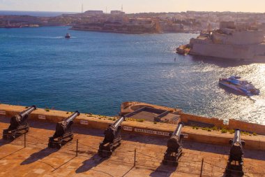 Valletta, Malta - February 13, 2024:  Cannons of the Saluting Battery point out over the Grand Harbour and Fort St Angelo, on a clear morning, Upper Barrakka Gardens, Capital city of Malta, clipart