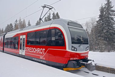 Strbske Pleso, Slovakya - 16 Aralık 2024: Slovakya 'daki Strbske Pleso' nun karlı tren istasyonunda yolcuları bekleyen modern elektrikli tren dağ parkı High Tatras 'ta..