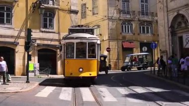 Lizbon, Portekiz - 27 Temmuz 2025: Klasik bir ünlü sarı tramvay Lizbon 'daki canlı kırmızı tarihi binalardan sabah erken saatlerde geçiyor