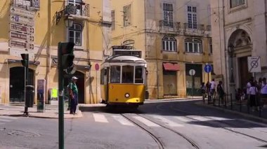 Lizbon, Portekiz - 27 Temmuz 2025: Klasik bir ünlü sarı tramvay Lizbon 'daki canlı kırmızı tarihi binalardan sabah erken saatlerde geçiyor