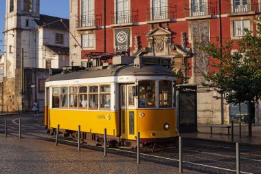 Lizbon, Portekiz - 27 Temmuz 2025: Klasik bir ünlü sarı tramvay Lizbon 'daki canlı kırmızı tarihi binalardan sabah erken saatlerde geçiyor