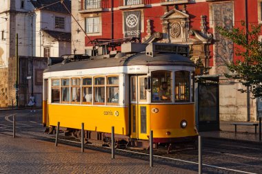 Lizbon, Portekiz - 27 Temmuz 2025: Klasik bir ünlü sarı tramvay Lizbon 'daki canlı kırmızı tarihi binalardan sabah erken saatlerde geçiyor