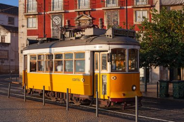 Lizbon, Portekiz - 27 Temmuz 2025: Klasik bir ünlü sarı tramvay Lizbon 'daki canlı kırmızı tarihi binalardan sabah erken saatlerde geçiyor