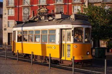 Lizbon, Portekiz - 27 Temmuz 2025: Klasik bir ünlü sarı tramvay Lizbon 'daki canlı kırmızı tarihi binalardan sabah erken saatlerde geçiyor