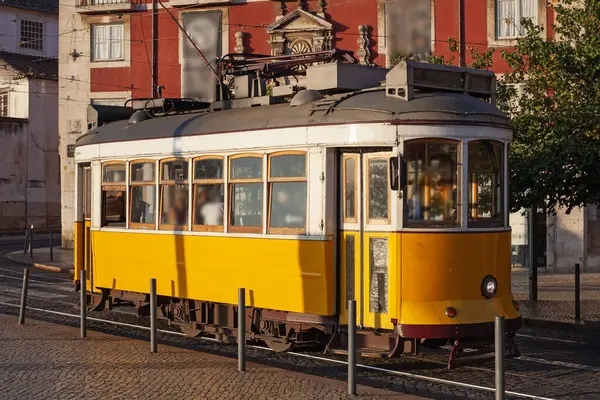 Lizbon, Portekiz - 27 Temmuz 2025: Klasik bir ünlü sarı tramvay Lizbon 'daki canlı kırmızı tarihi binalardan sabah erken saatlerde geçiyor