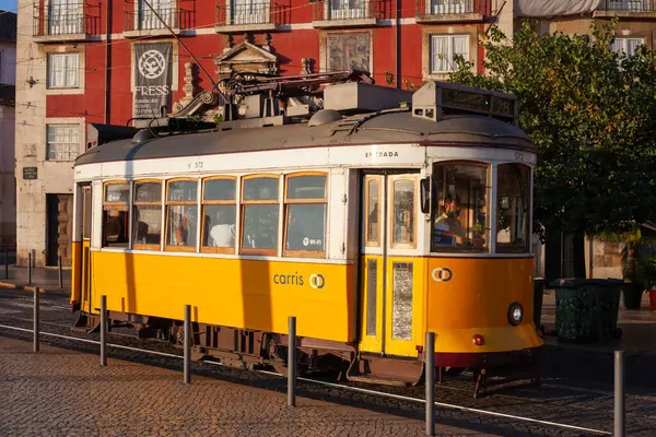 Lizbon, Portekiz - 27 Temmuz 2025: Klasik bir ünlü sarı tramvay Lizbon 'daki canlı kırmızı tarihi binalardan sabah erken saatlerde geçiyor
