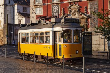 Lizbon, Portekiz - 27 Temmuz 2025: Klasik bir ünlü sarı tramvay Lizbon 'daki canlı kırmızı tarihi binalardan sabah erken saatlerde geçiyor