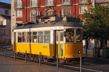 Lizbon, Portekiz - 27 Temmuz 2025: Klasik bir ünlü sarı tramvay Lizbon 'daki canlı kırmızı tarihi binalardan sabah erken saatlerde geçiyor