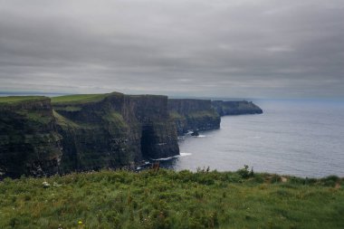 İrlanda 'daki Moher Kayalıkları' nın engebeli kıyı şeridi ve bulutlu gökyüzü manzarası