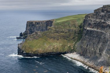 İrlanda 'daki Moher Kayalıkları' nın engebeli kıyı şeridi ve bulutlu gökyüzü manzarası