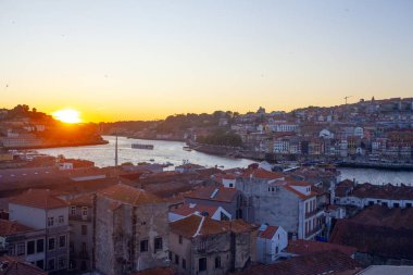 Porto 'nun tarihi mimarisi ve hareketli nehrinin sıcak bir günbatımı manzarası.