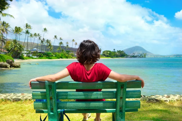 ハワイの海に沿って公園のベンチに座っている若い女性 バックグラウンドでココヘッドクレーター — ストック写真