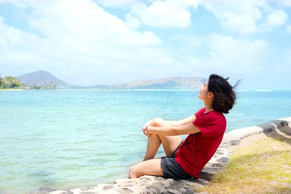 ハワイ州オアフ島沖の海水沿いの岩壁に座っている若い女性 — ストック写真
