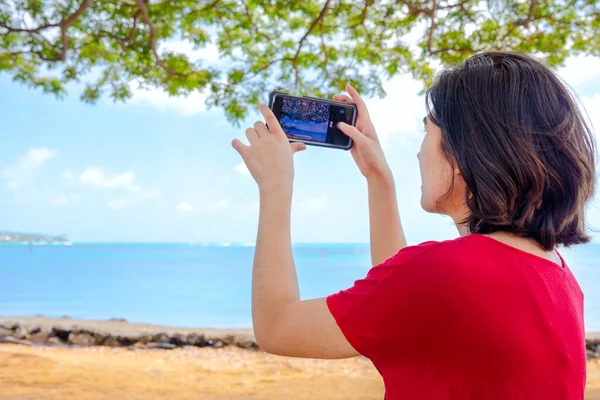 ハワイの海で写真を撮るために携帯電話を使う若い女性 — ストック写真