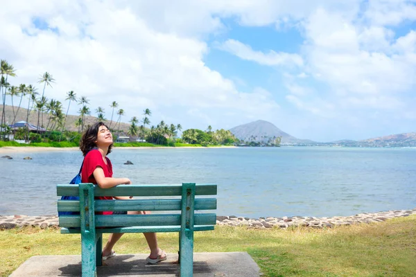 ハワイの海に沿って公園のベンチに座っている若い女性 バックグラウンドでココヘッドクレーター — ストック写真