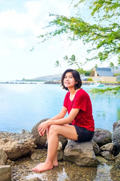 日陰の木の下のハワイの海の静かな湾の大きな岩の上に座ってリラックスしている若い女性 — ストック写真