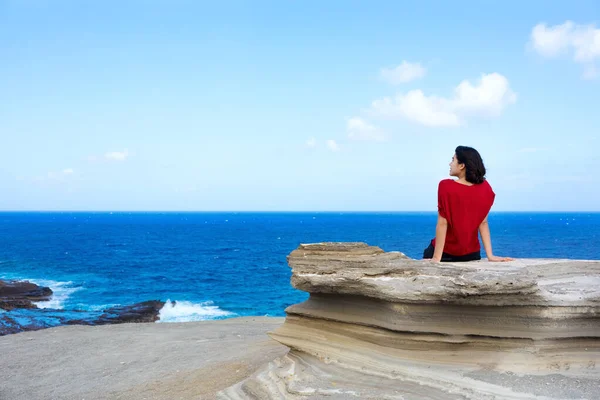ハワイの海の大きな岩の崖に座って地平線を眺めている若い女性 — ストック写真