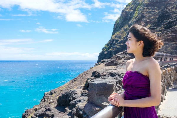 站在夏威夷瓦胡岛的Makapu Viewpoint 俯瞰Makapu U海滩和夏威夷海的身着正式紫色衣服的年轻女子 免版税图库照片