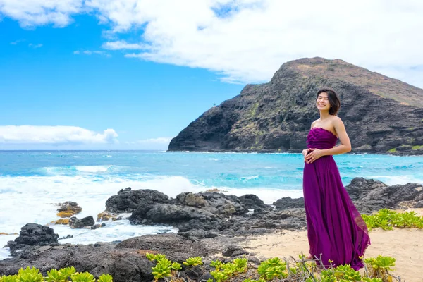 マカプーのビーチでハワイの海岸の岩のビーチに立っている紫色のドレスのティーンガール ストック画像
