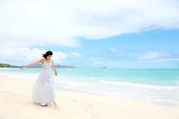 青い太平洋でハワイのビーチで裸足を歩く白いドレスのティーンガール ロイヤリティフリーのストック写真