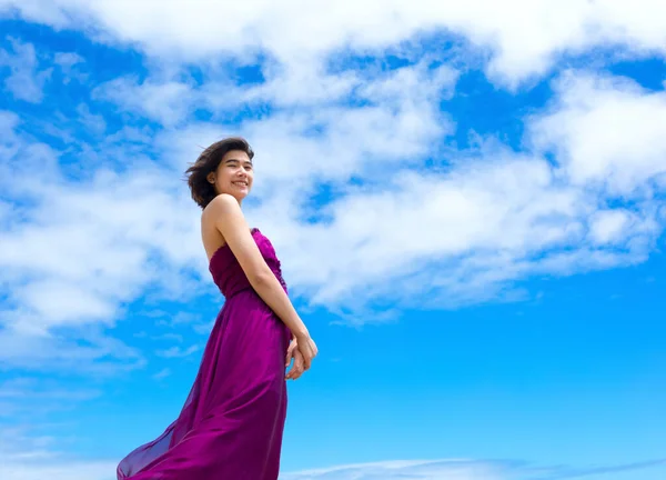 青い空に立っている紫色のドレスのティーンガール ストック写真