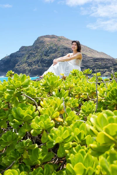 身着白衣的少女坐在夏威夷海岸Makapu U海滩的熔岩上 图库图片
