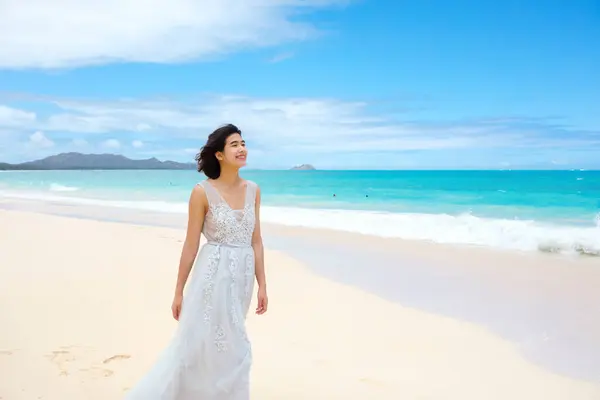 穿着白衣的少女走在太平洋蓝色海岸旁的夏威夷海滩上 免版税图库照片