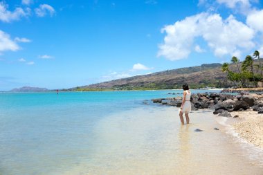 Hawaii 'nin sığ ve berrak sularında yürüyen beyaz elbiseli genç kız.
