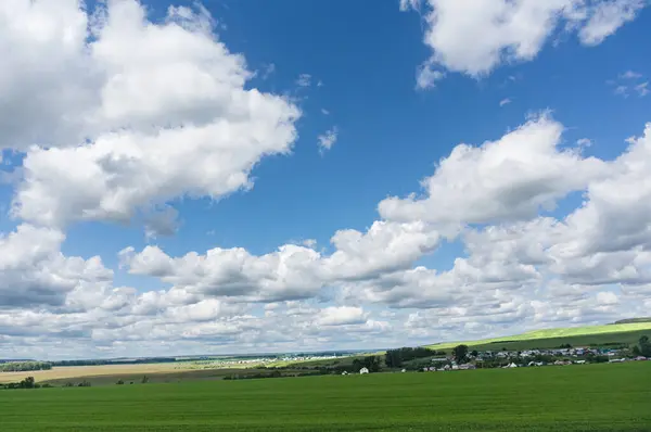 蓝天高耸 云朵蓬松 夏天青绿的草场 地平线上的村庄 在全国各地放松旅行的概念 图库图片