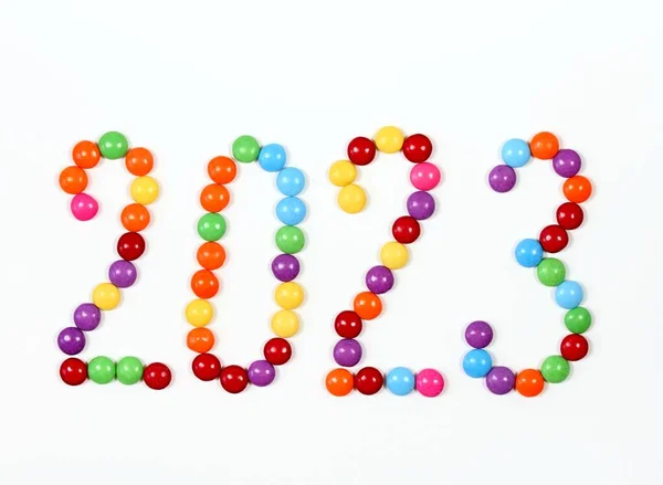 Year 2023, colorful smarties on white background. Chocolate candies in a shape of buttons, top view.