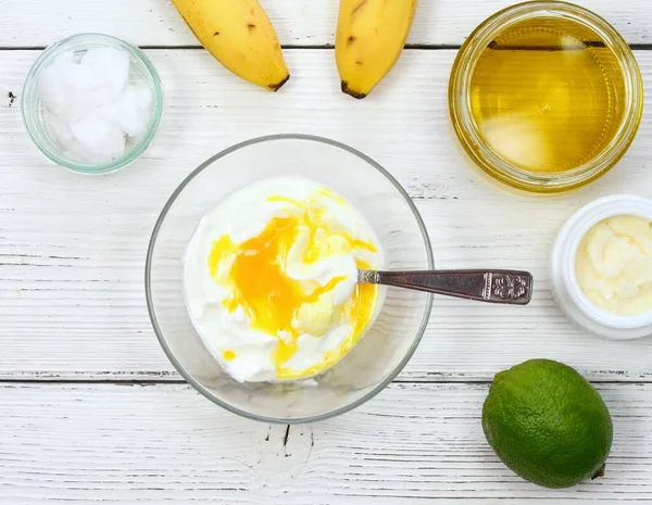 Natural ingredients for smoothing, softening and hydrating hair. Banana, lime, yogurt, shea butter, egg yolk, coconut and olive oil for hair mask, flat lay.
