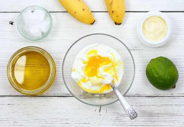 Natural ingredients for smoothing, softening and hydrating hair. Banana, lime, yogurt, shea butter, egg yolk, coconut and olive oil for hair mask, flat lay.