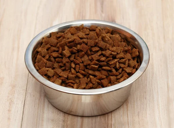 Bowl of pets food i the bowl. Full bowl of cat or dog dried food on wooden table.